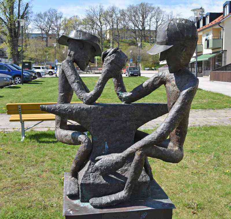 Staty som föreställer två män som bryter arm över ett städ. 