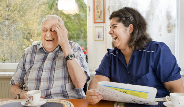 Äldre man och kvinna från hemtjänst skrattar tillsammans.