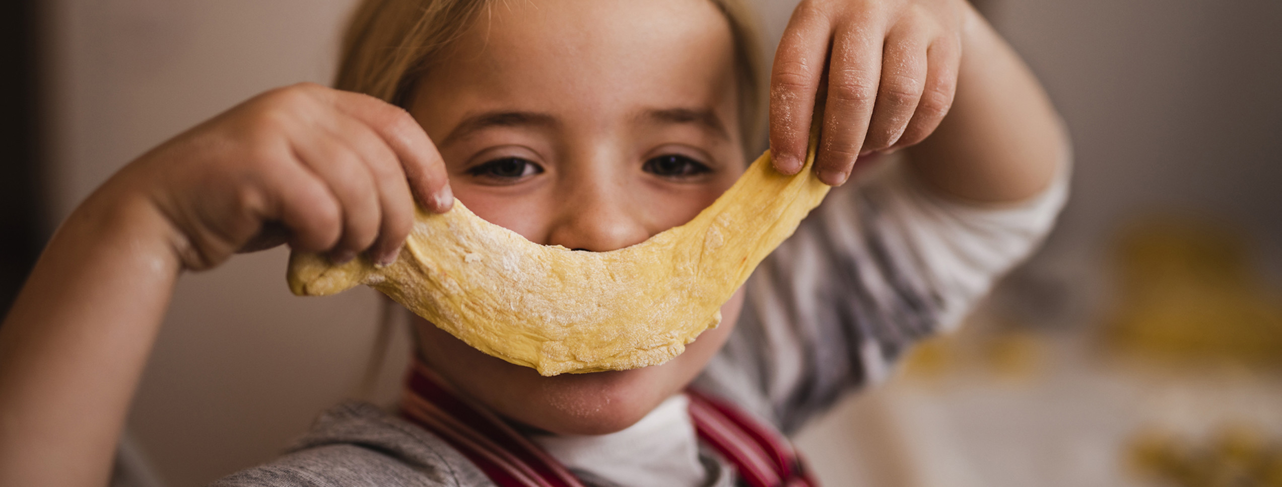 Barn som bakar lussebullar och håller upp en bit deg som en glad mun.