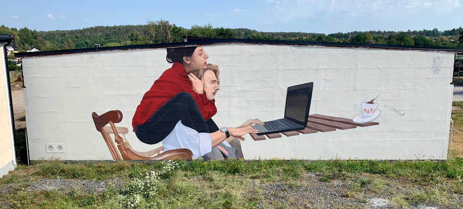Väggmålning föreställande en kvinna som sitter på en mans axlar framför en dator. 
