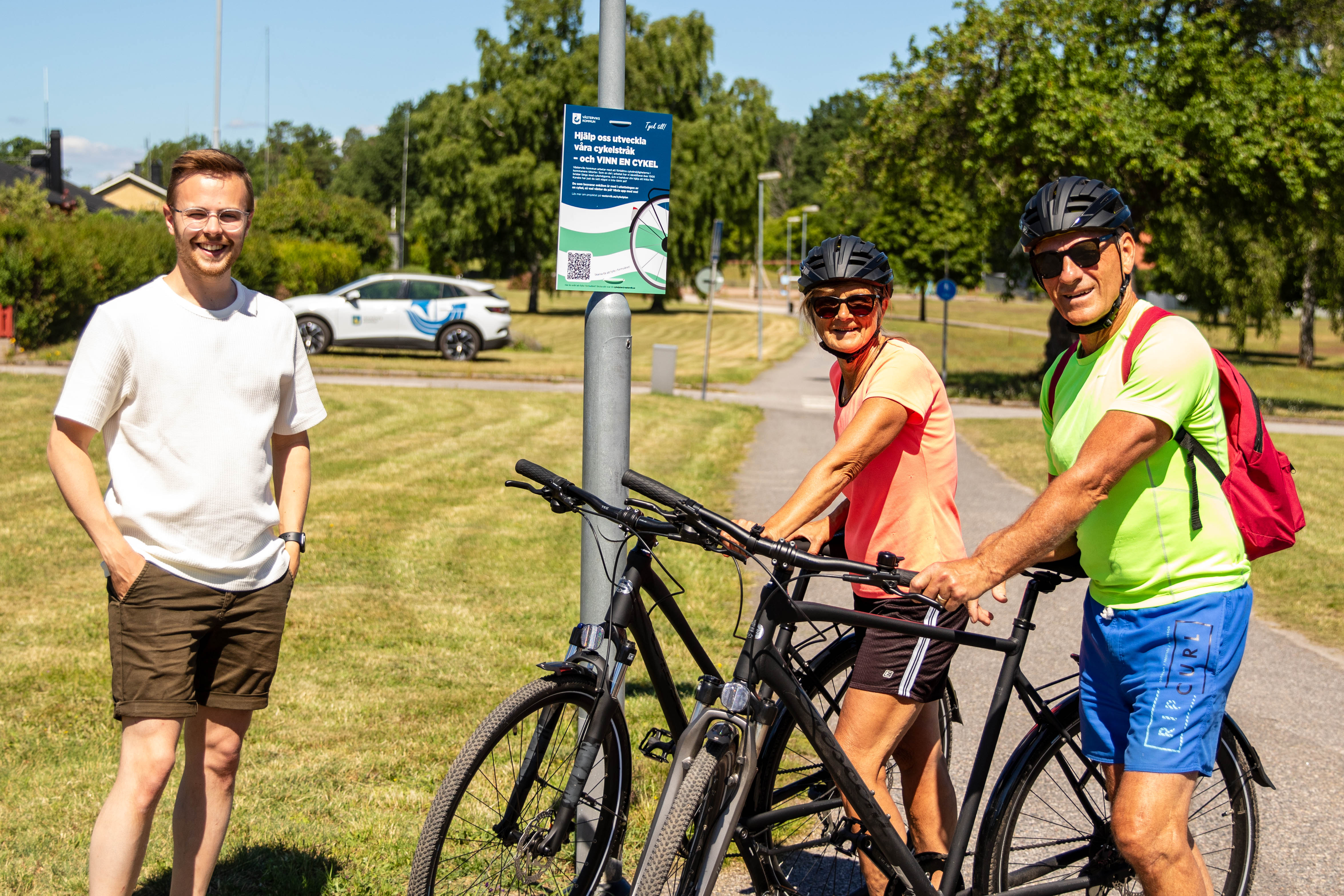 Projektledaren Sebastian Wadenborg ler mot kameran bredvid två medborgare som ställer frågor om "cykelskylten".