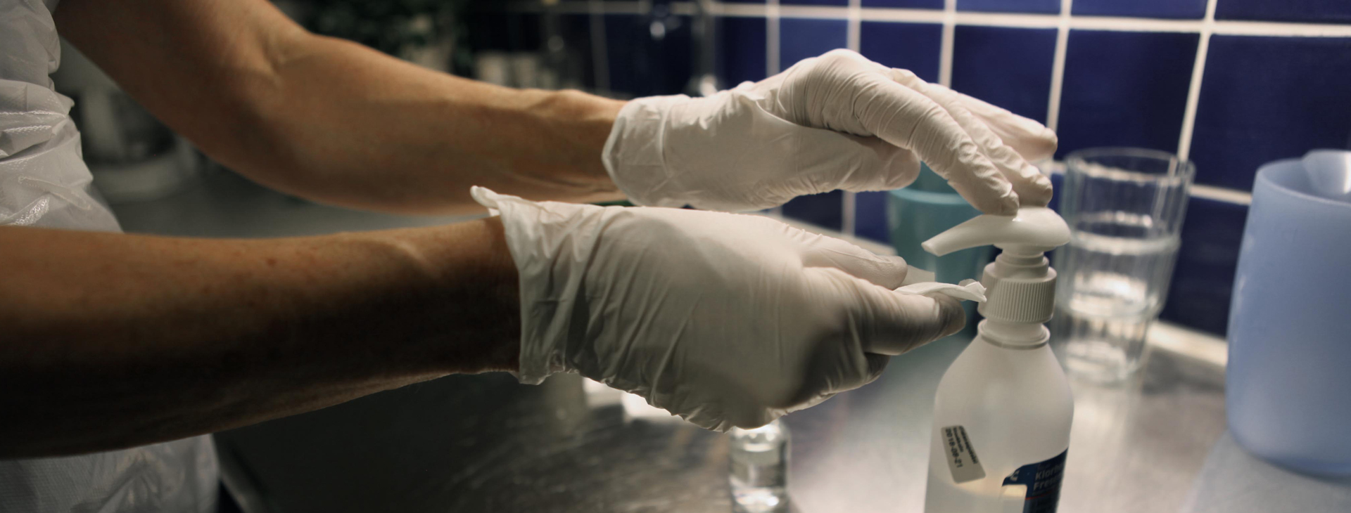 Bild på två händer med vita plasthandskar, som trycker ut desinfektionsmedel på en bommulspad.
