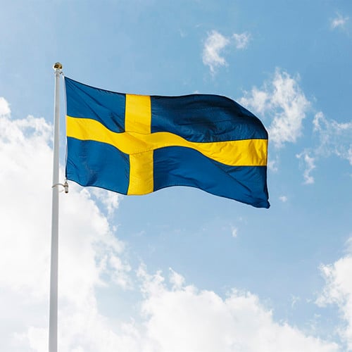 Svensk flagga mot blå himmel med vita moln.