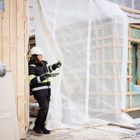 Kvinna på byggarbetsplats som står med en ritning och pekar.