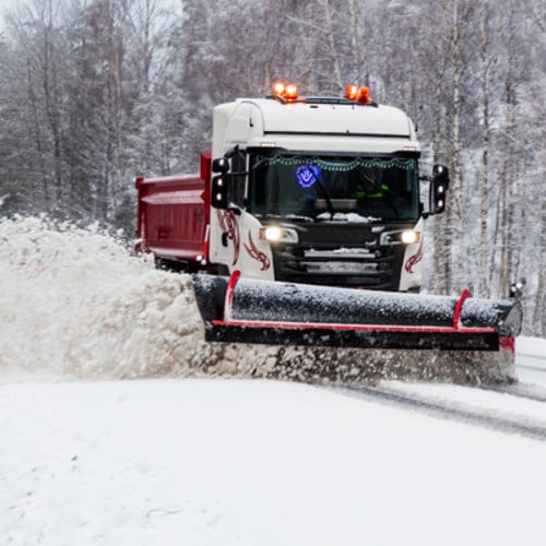 Plogbil som kör på en igensnöad väg.