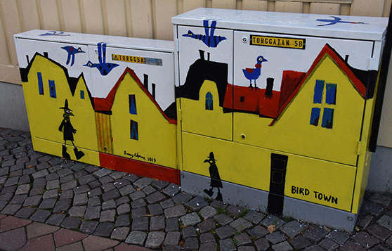 Konstverk med gula hus och svarta fåglar i hatt