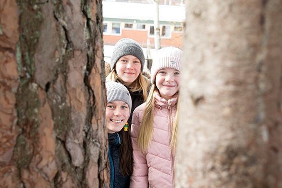 Kaia, Sofia och Julia tittar fram bakom trädstammar